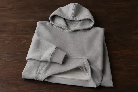 Sweat à capuche en molleton plié sur du bois foncé, avec poche kangourou et poignets côtelés.
