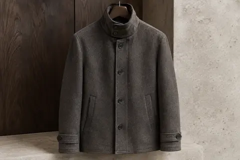 Manteau court pour homme à col montant boutonné, présenté seul sur un cintre dans un décor épuré.