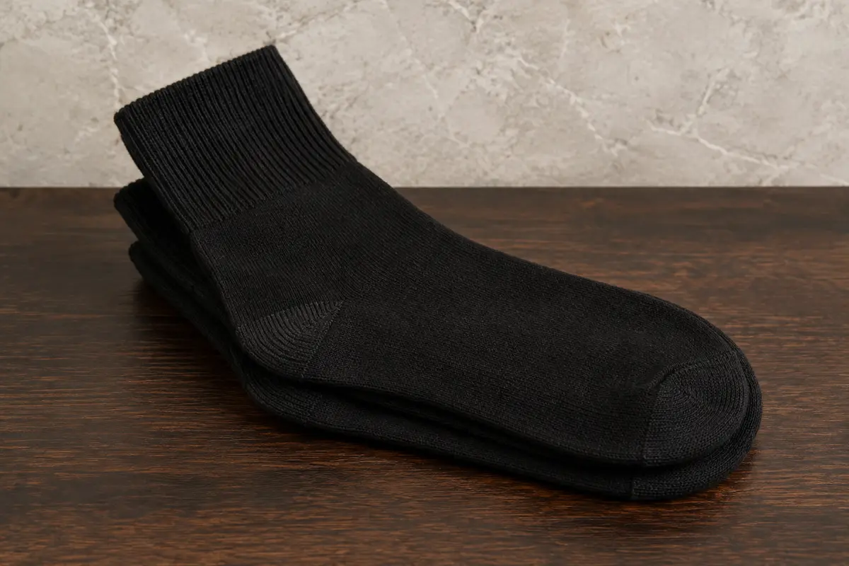 Paire de chaussettes noires mi-mollet en maille unie, pliées sur une surface en bois foncé.