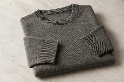 Pull homme en coton à col rond, plié sur une surface de pierre claire dans un décor éditorial épuré.